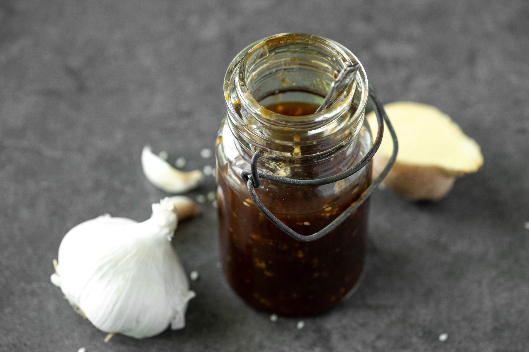 Glass jar filled with teriyaki sauce with a clove of garlic and a piece of ginger beside the jar.