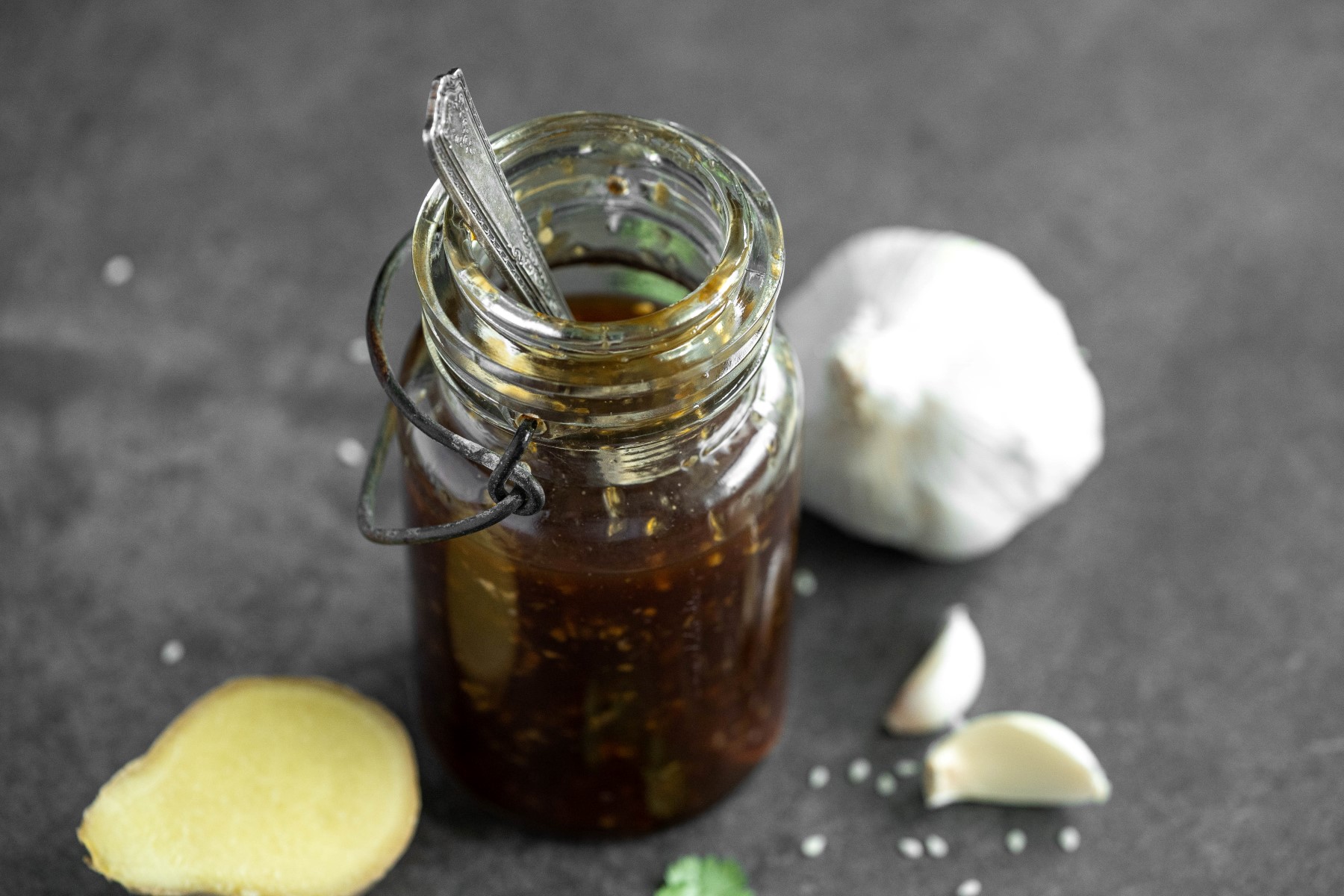 Glass jar filled with homemade teriyaki sauce with fresh garlic and fresh ginger beside the jar.