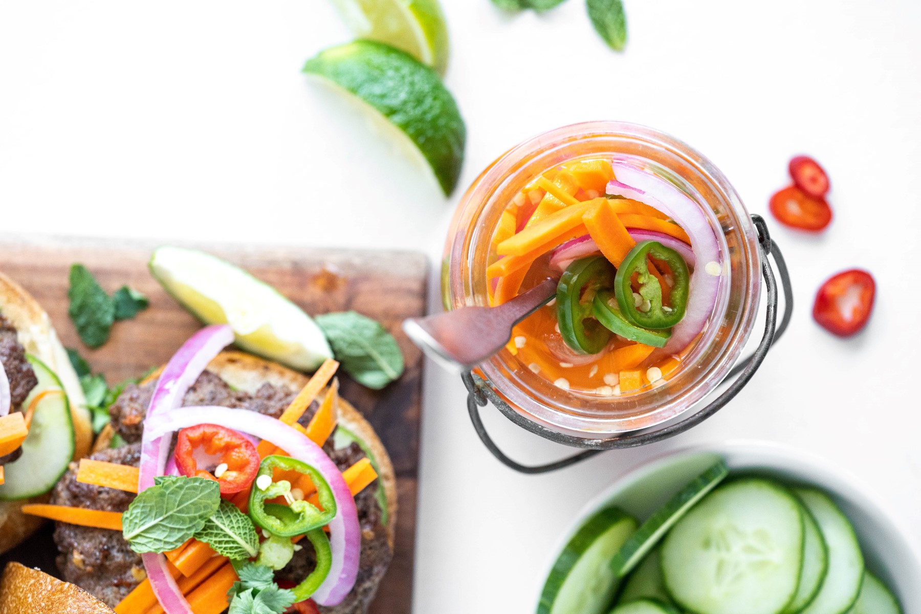 Quick pickled vegetables in a sealable glass jar beside a burger topped with pickled veggies.