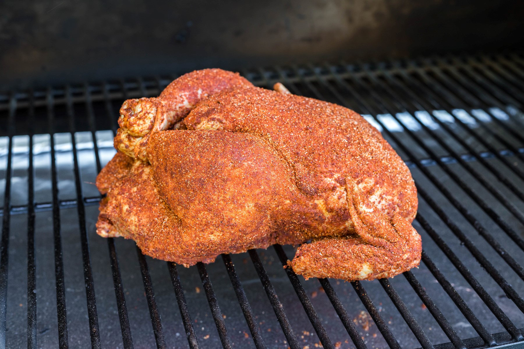 Whole chicken covered in dry rub on the smoker grill ready to start smoking.