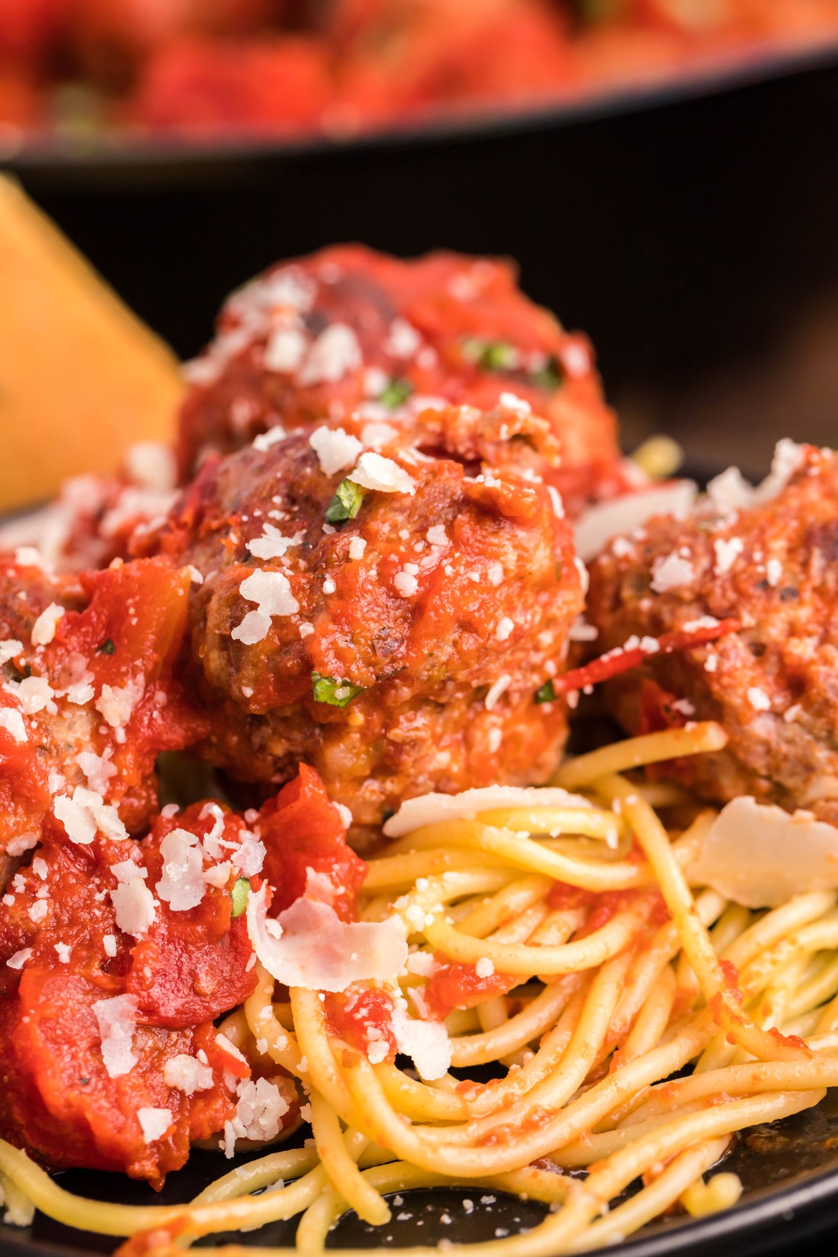 Smoked meatballs and tomato sauce on top of a plate of spaghetti garnished with parmesan cheese.
