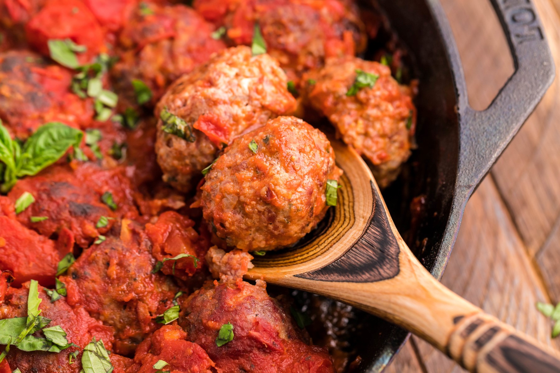 Scooping meatballs out of the cast iron skillet with a wooden spoon.