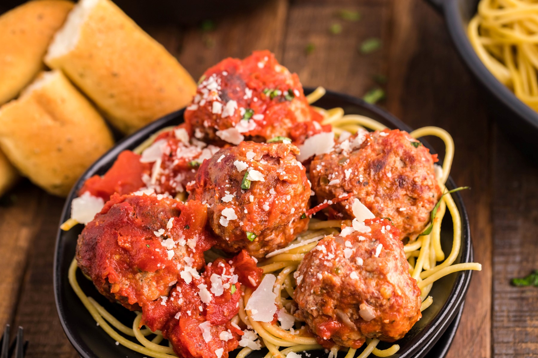 Meatballs served on top of spaghetti with bread on the side and grated parmesan on top