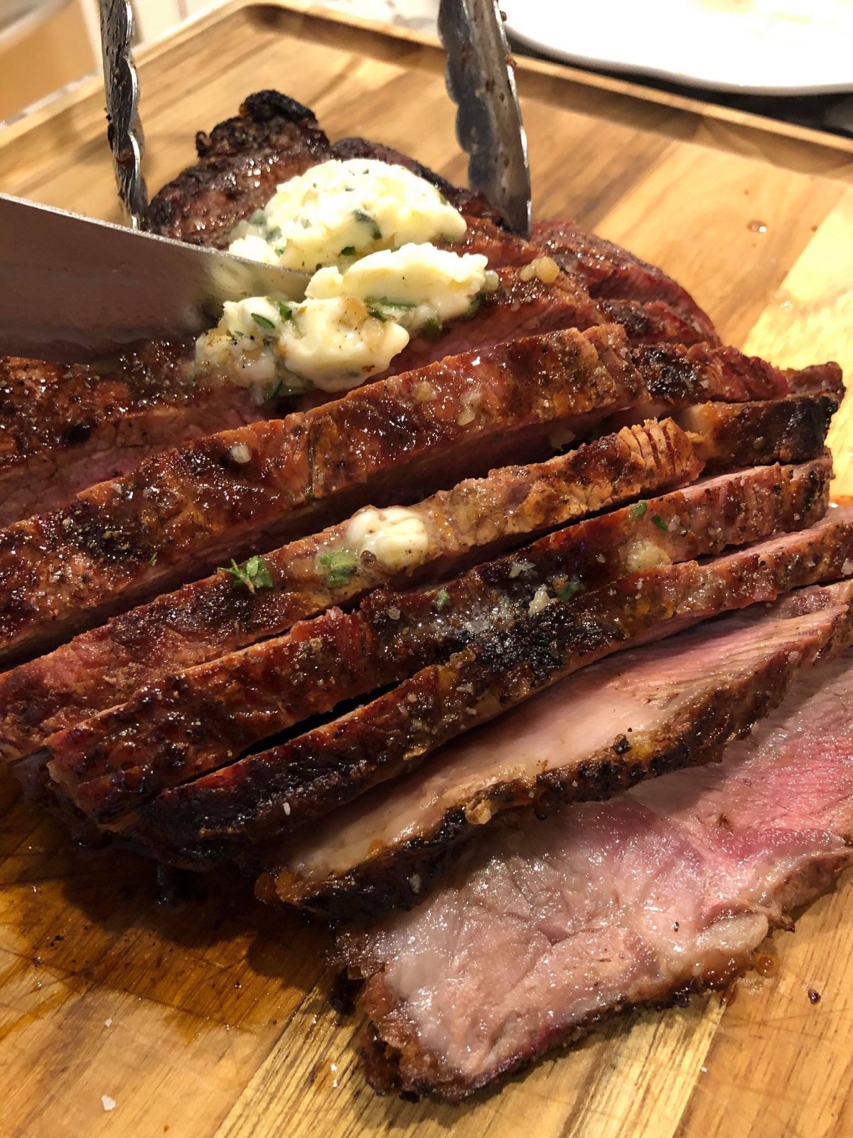 Grilled tomahawk steak being sliced on a wooden cutting board.