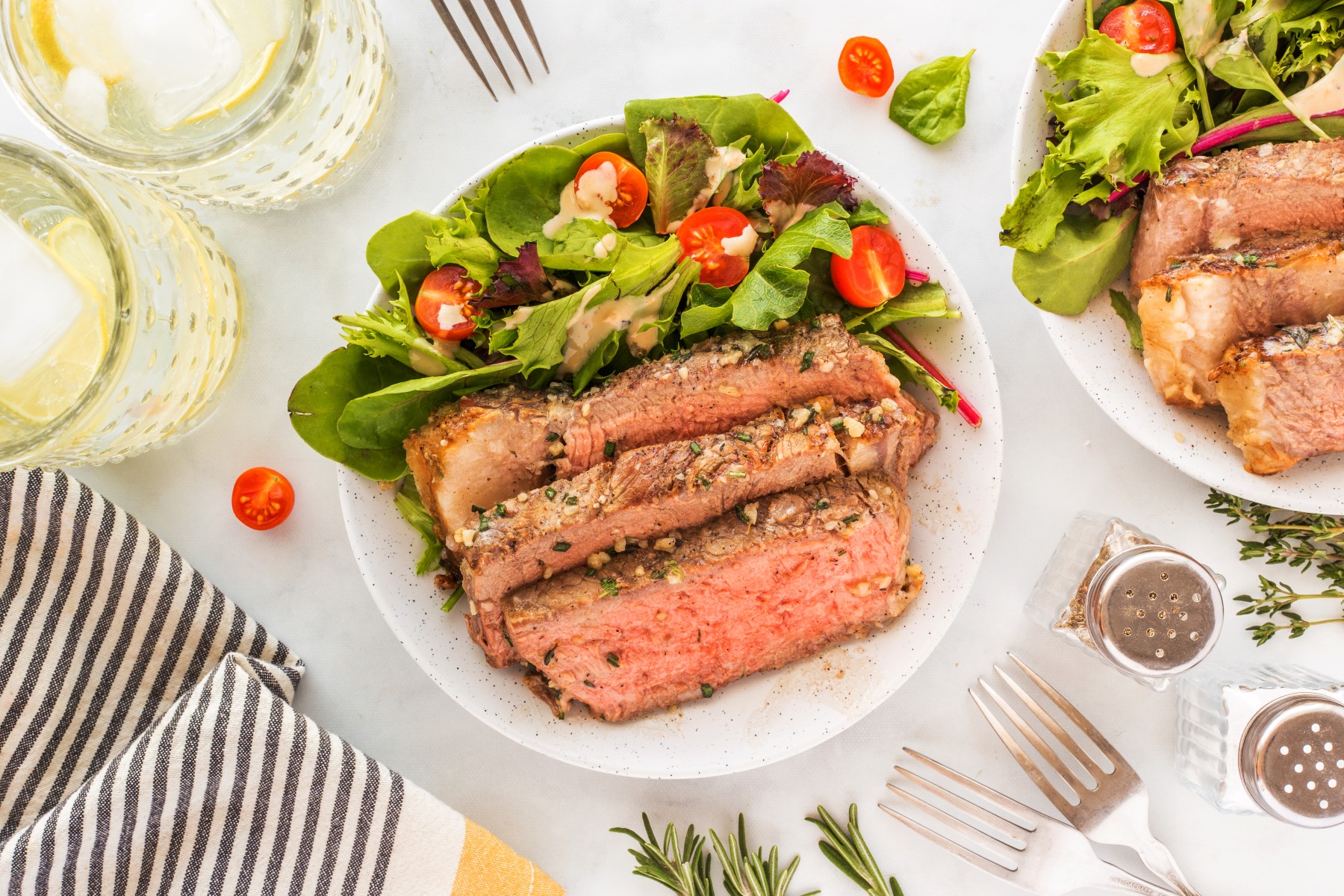 Slices of grilled tomahawk steak served on a white plate with a green salad.
