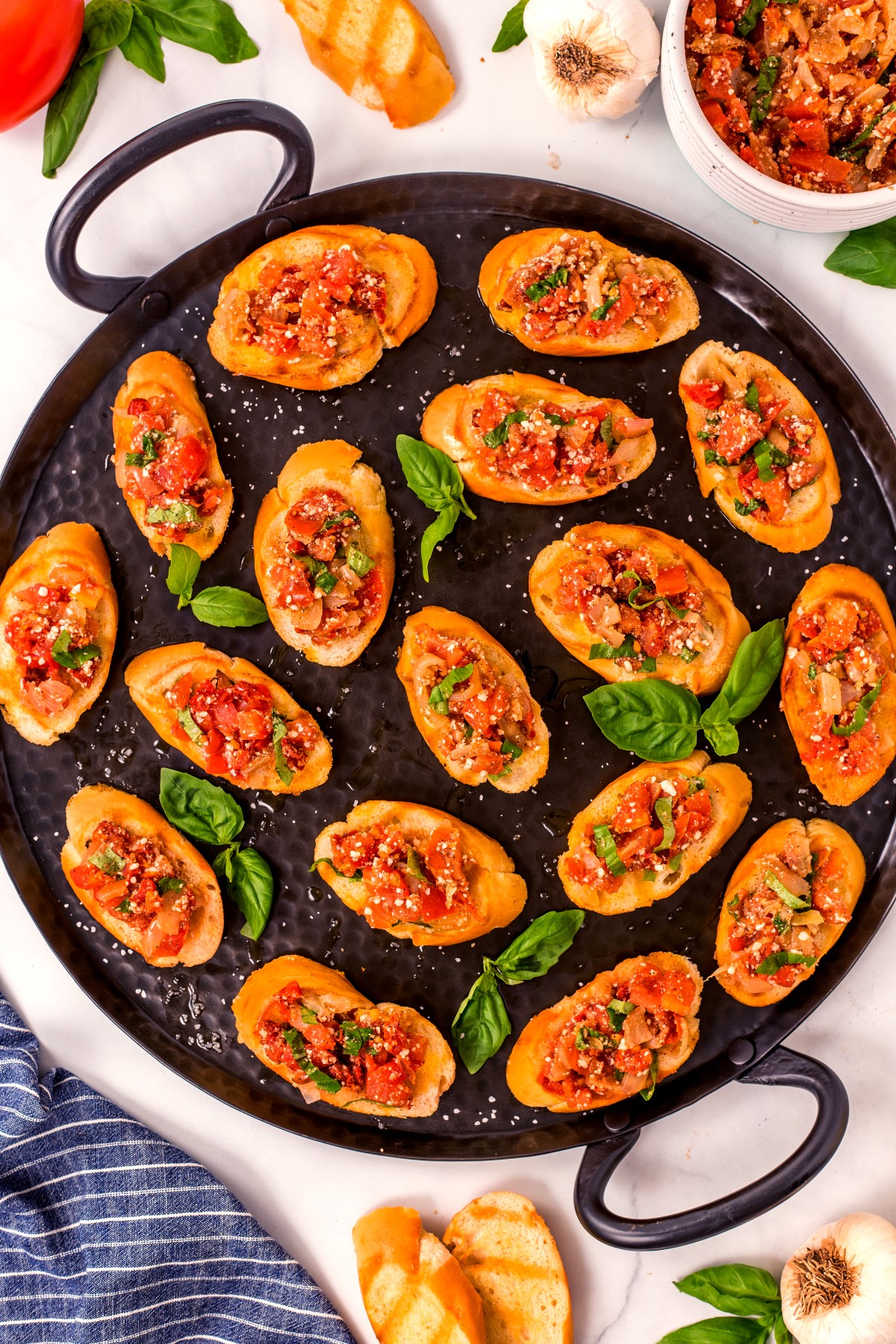 Bruschetta served on a round metal tray with fresh basil leaves as garnish
