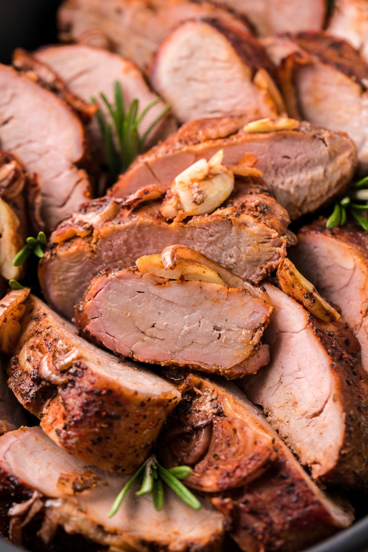 Slices of pork tenderloin with roasted garlic cloves, roasted shallots, and fresh rosemary.