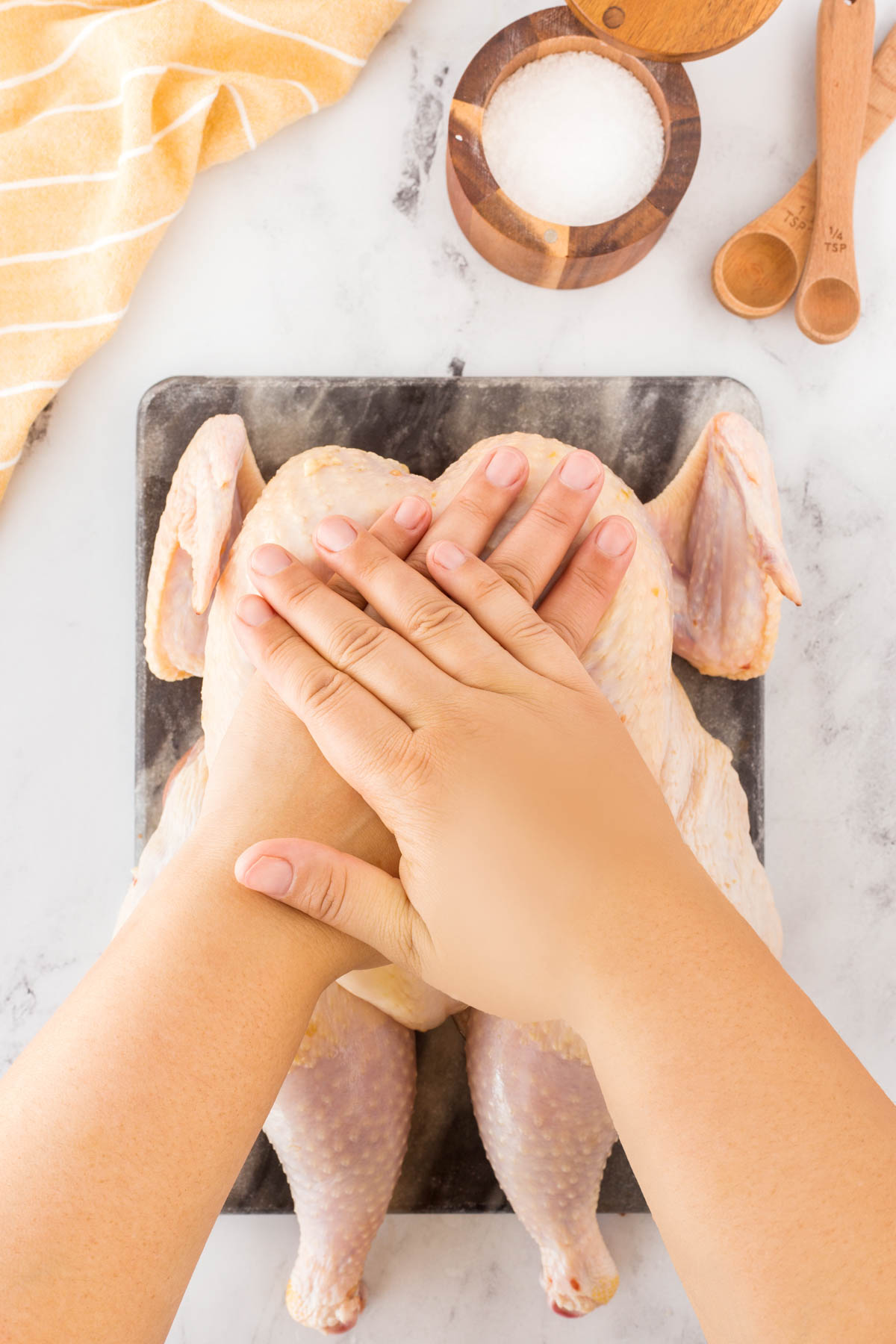 Hands cross over the top of the whole chicken while it sits on a cutting board.