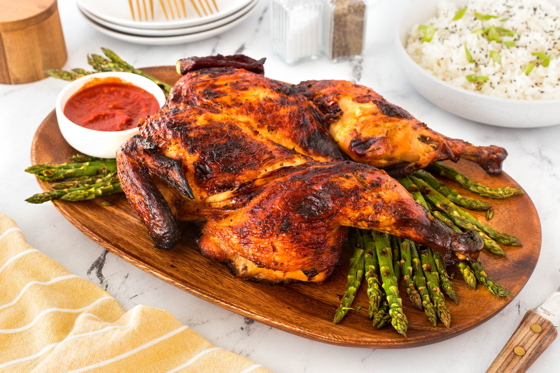 Spatchcock grilled Gochujang Chicken on a wooden cutting board with asparagus and dipping sauce.