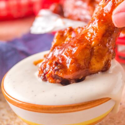 Crisp BBQ chicken wing being dipped into a bowl of ranch dressing.