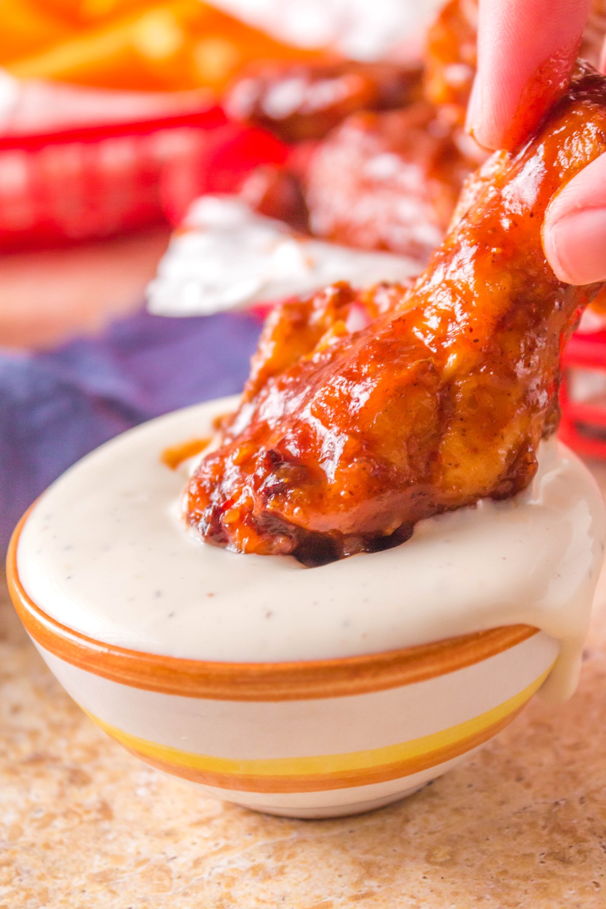 Crispy BBQ chicken wing covered in sauce being dipped into a ranch dipping sauce.