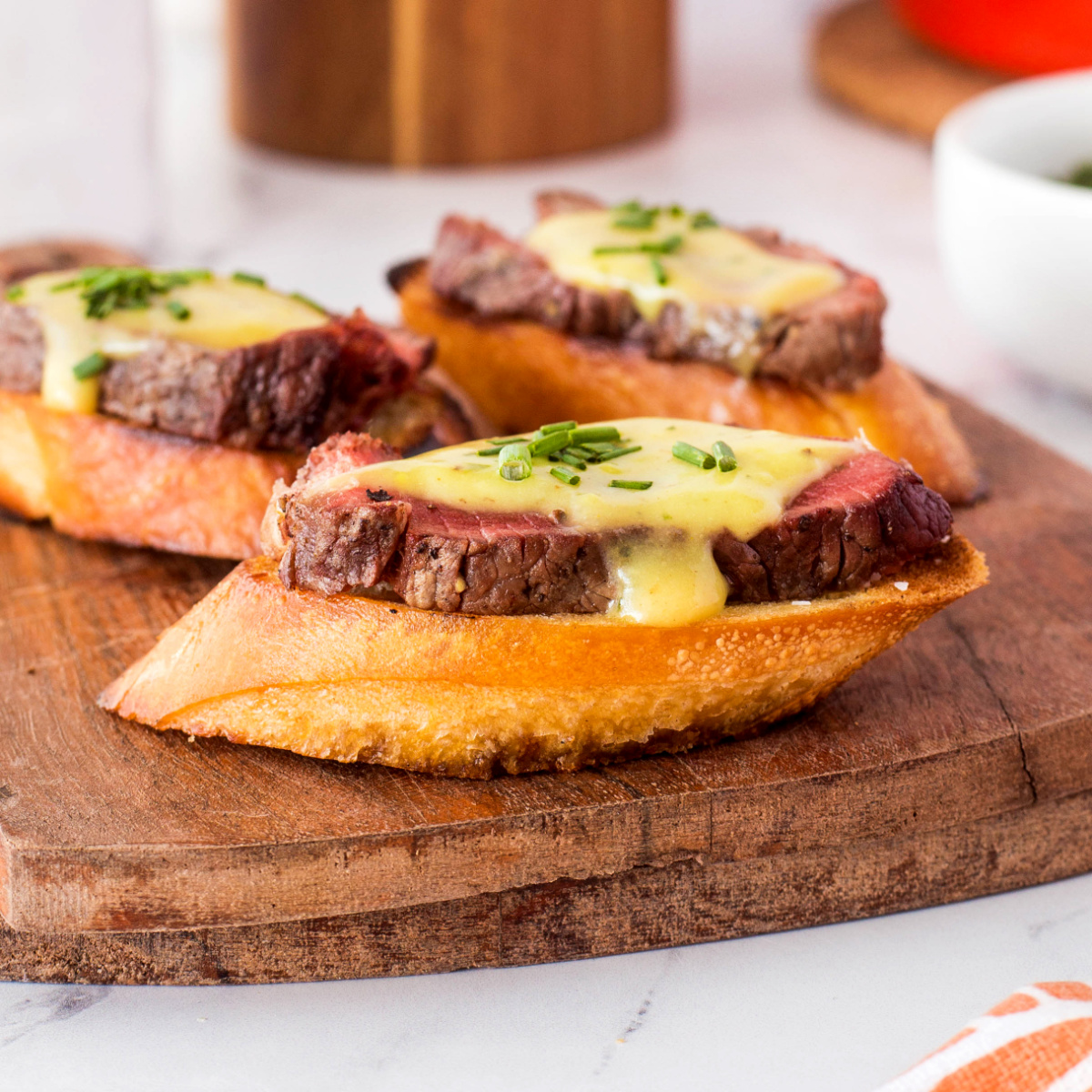 Grilled beef tenderloin crostini with béarnaise sauce and chives on a wooden board