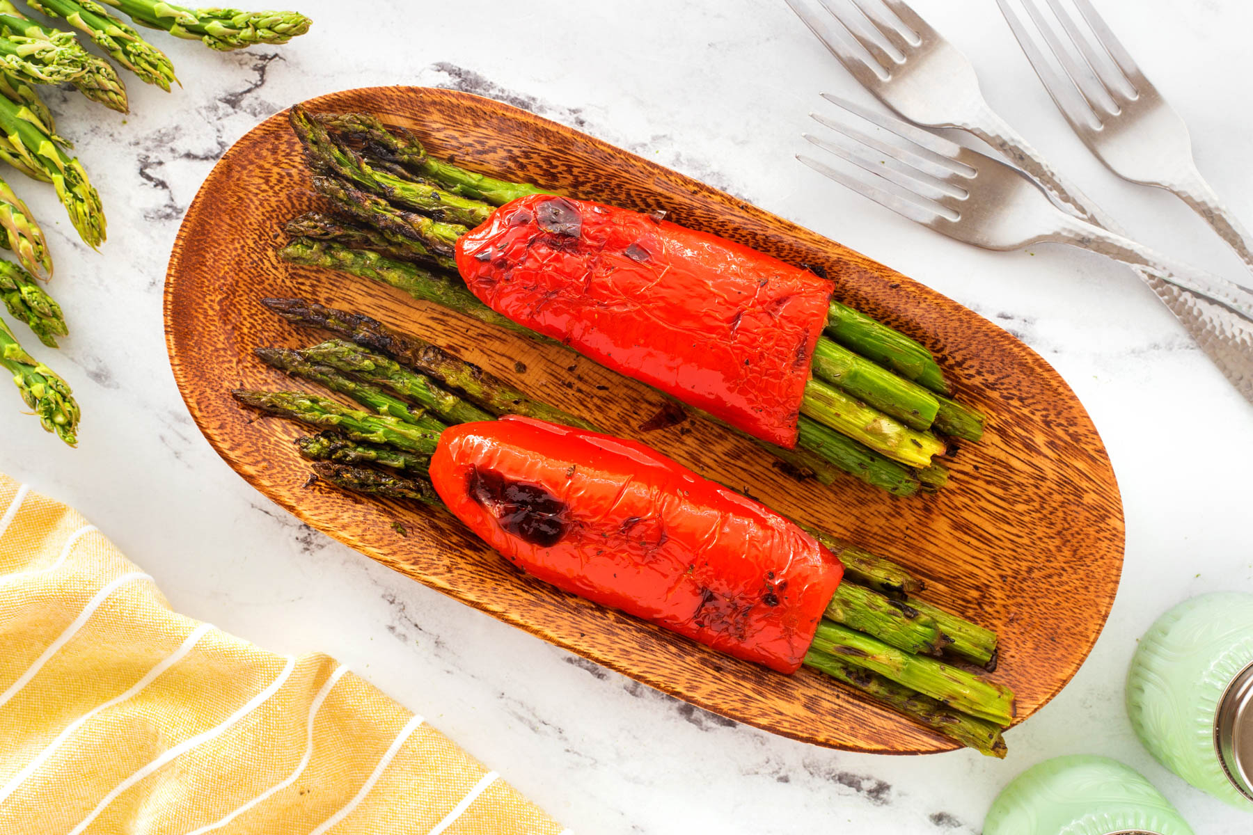 Grilled asparagus bundles on a wooden cutting board with some forks beside the board.