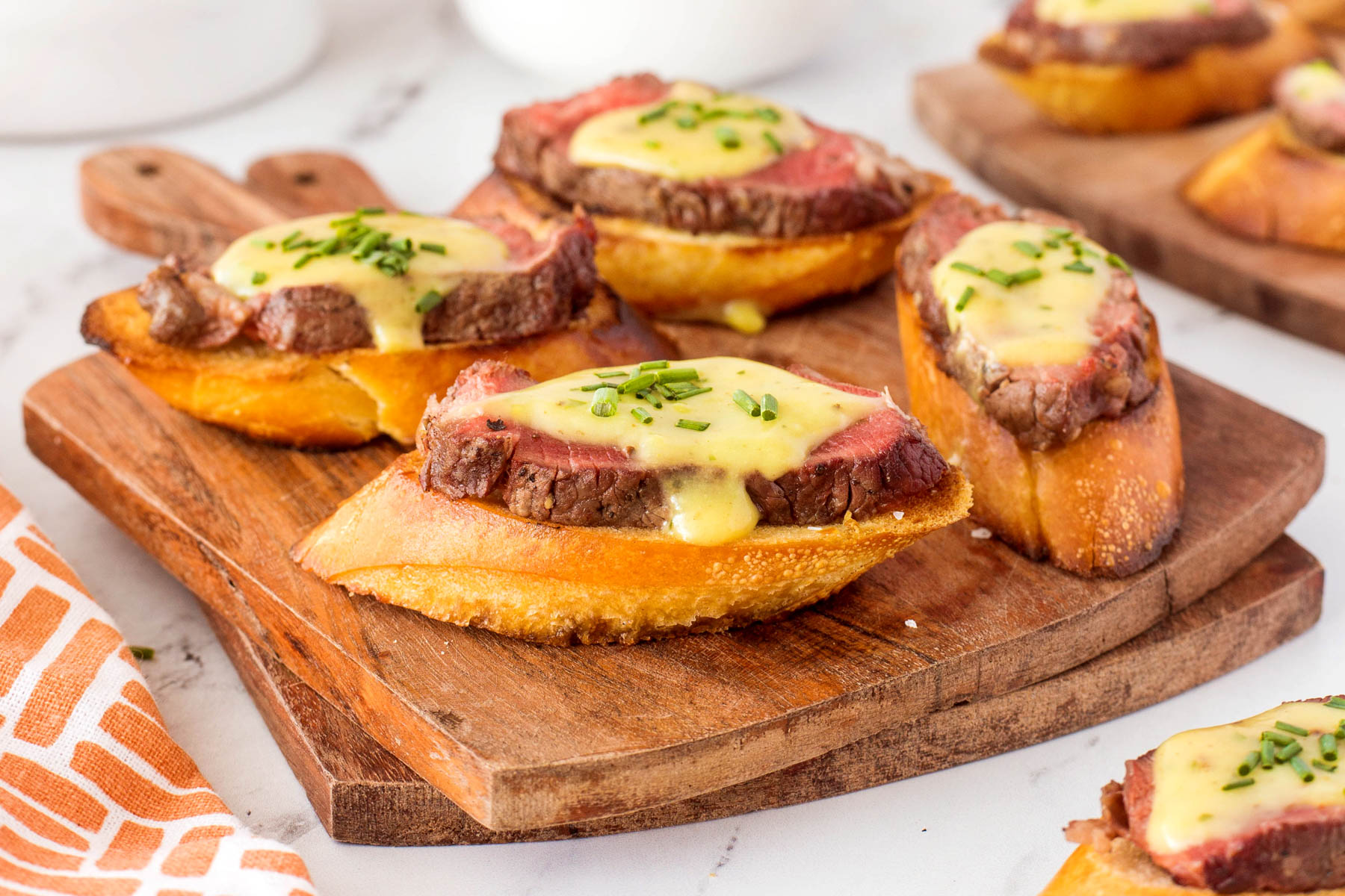 Grilled beef crostini with béarnaise sauce and chopped chives on a wooden serving board.