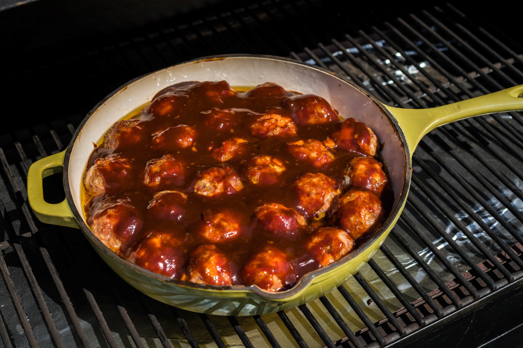 Meatballs covered in sauce in a cast iron skillet on the smoker grill.