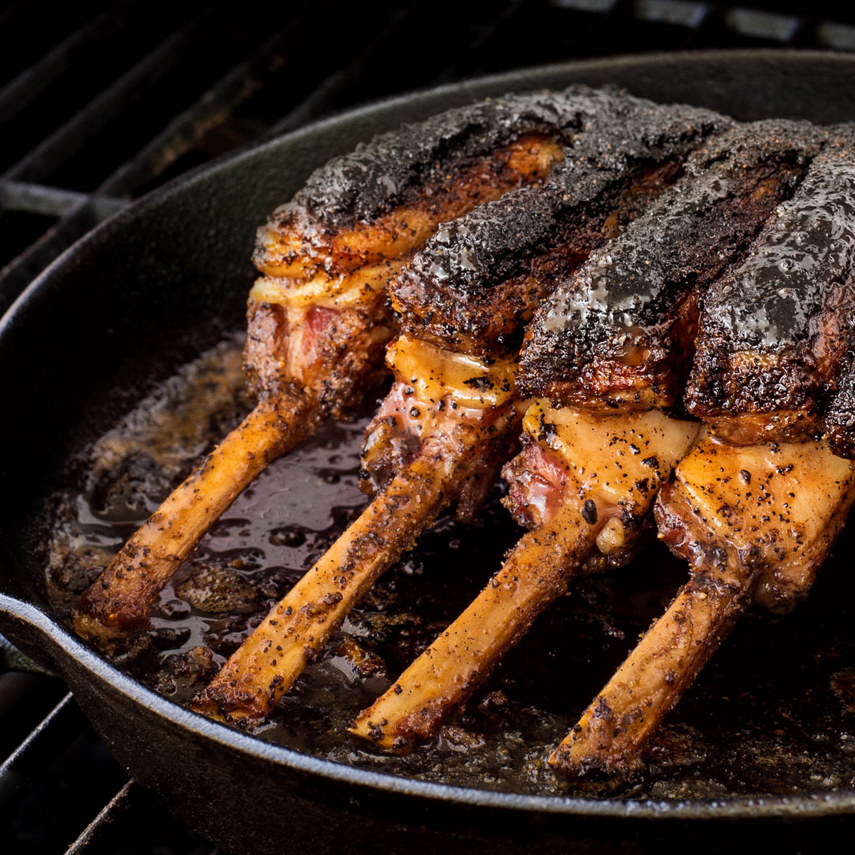 Rack of lamb cooking in a cast iron skillet on the grill.