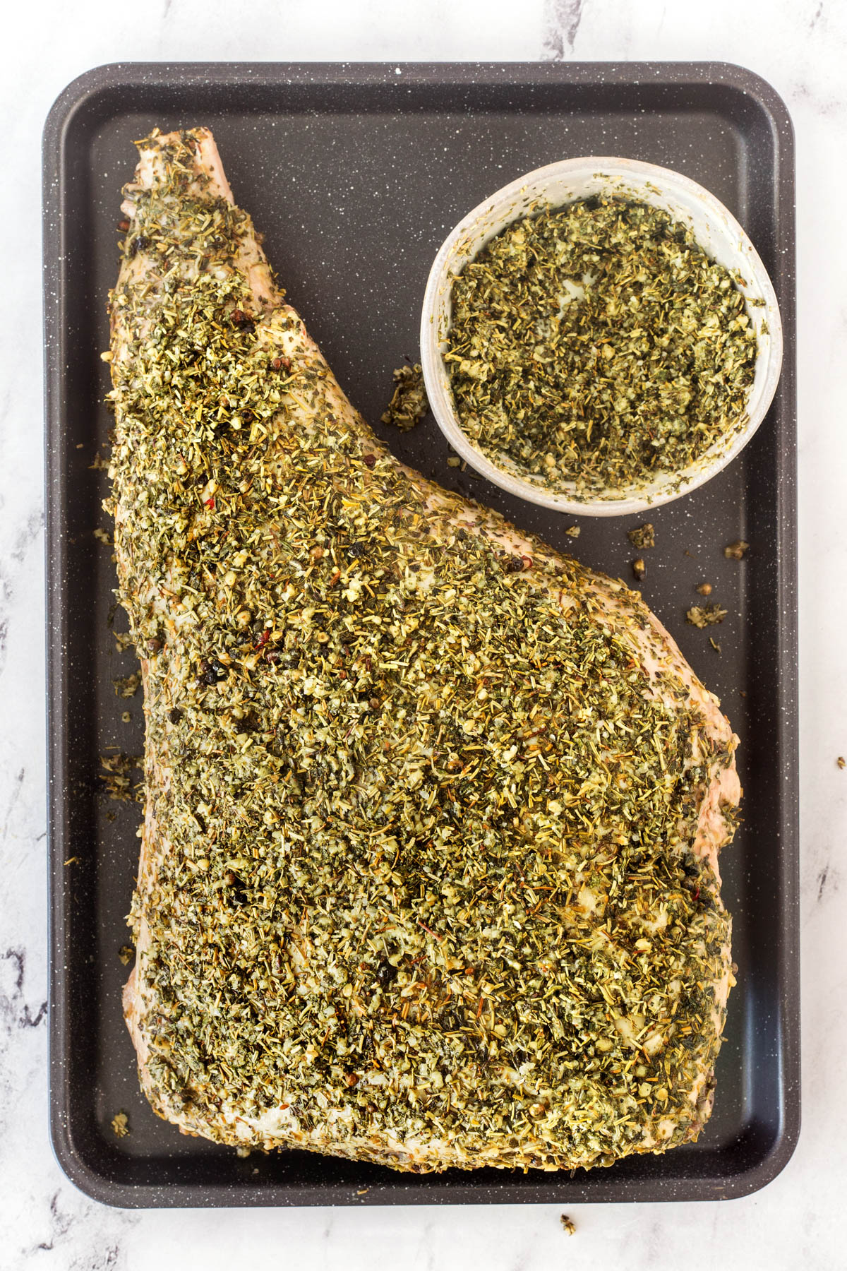 Leg of lamb rubbed with a generous coat of herbs on a baking sheet.