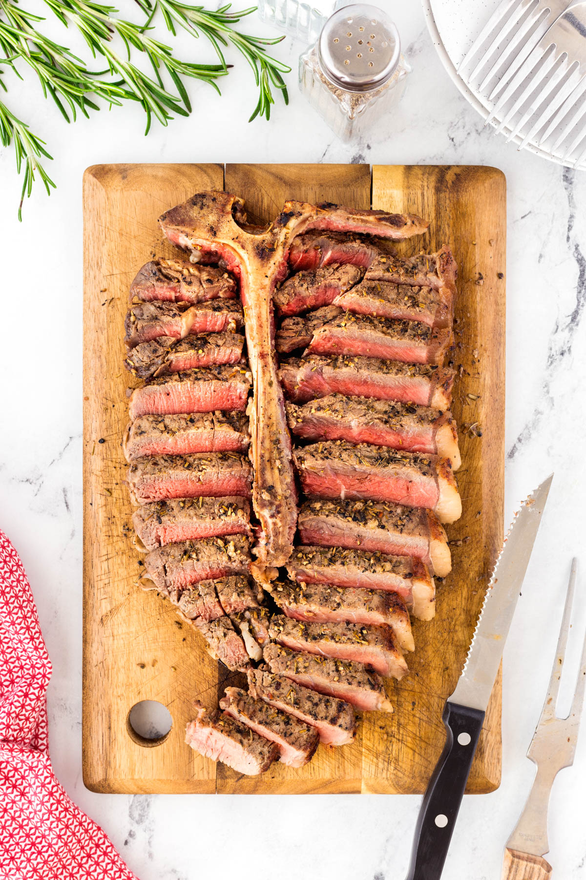 Grilled porterhouse steak sliced on a wooden cutting board and the meat replaced against the T-bone.