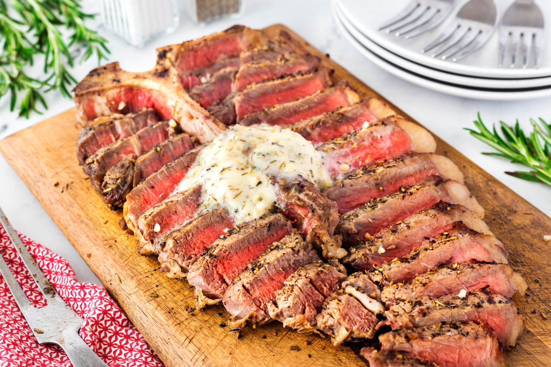 Grilled porterhouse steak sliced on a wooden cutting board and the meat replaced against the T-bone with a dollop of herb garlic butter melting on top.