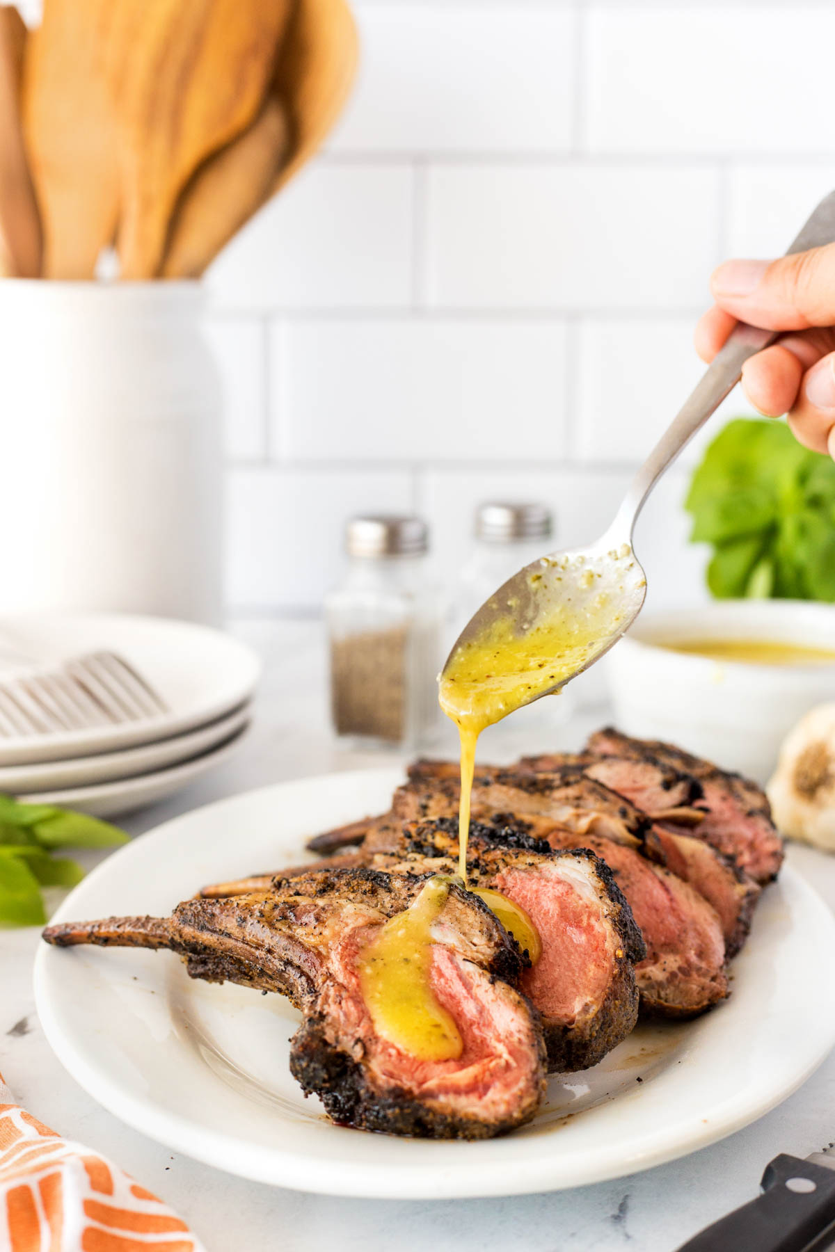 Rack of lamb cut into ribs on a platter and being drizzled with lemon garlic basil sauce.