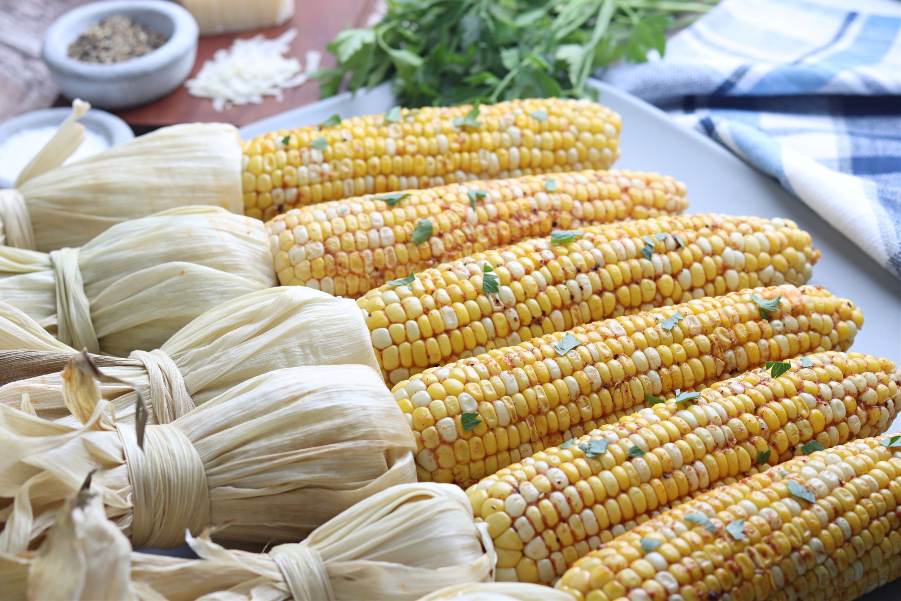Smoked corn on the cob husked and laid out on a  white platter garnished with chopped parsley