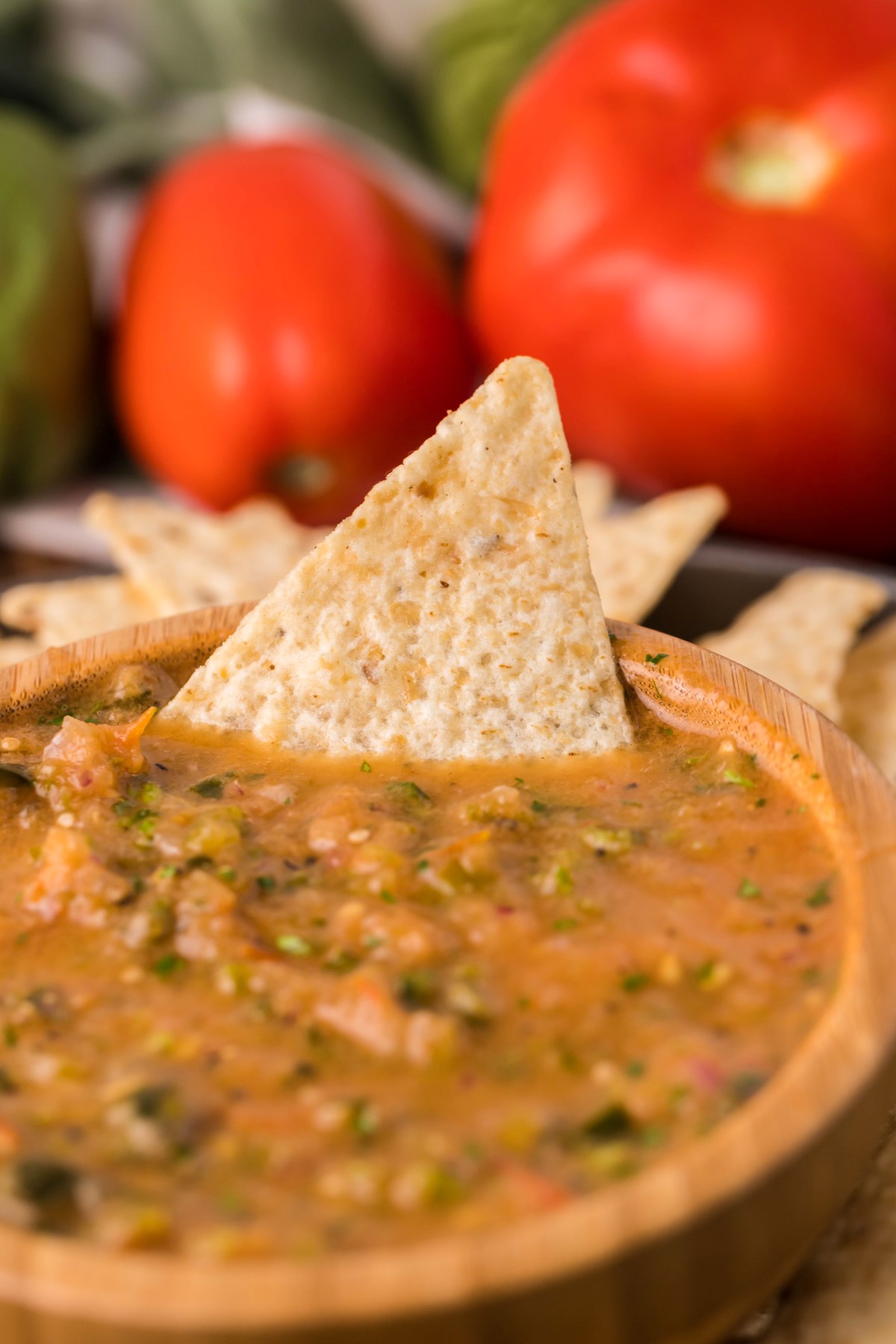 Smoked salsa in a wooden bowl with a tortilla chip dipped into the salsa