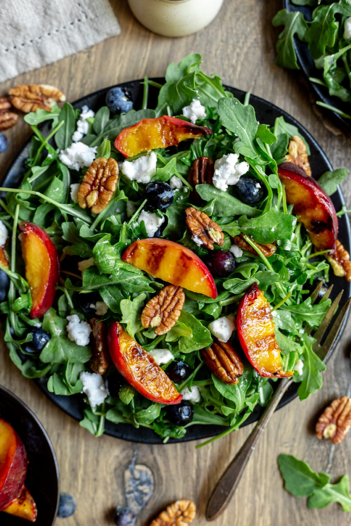 Grilled peach salad on a black plate with a fork