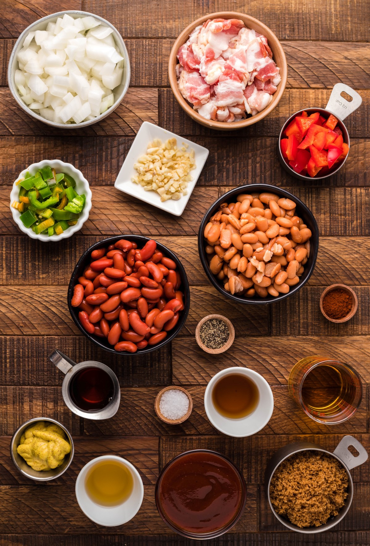 Ingredients for smoked baked beans laid out in bowls on a wooden table.