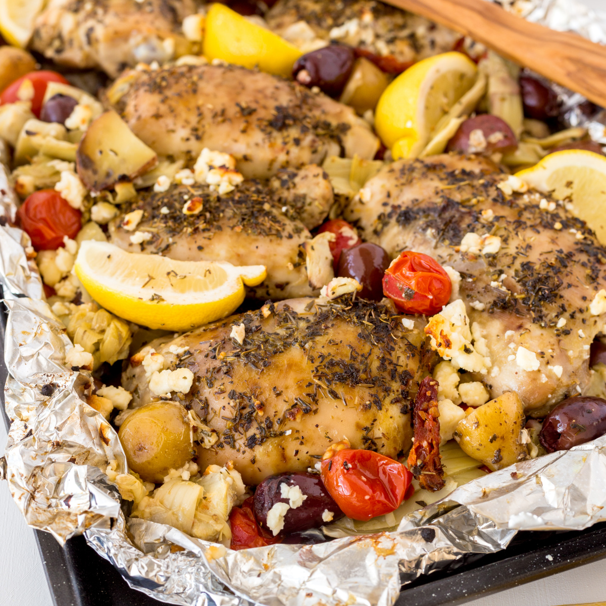 Greek chicken foil pack just off the grill garnished with lemon wedges.
