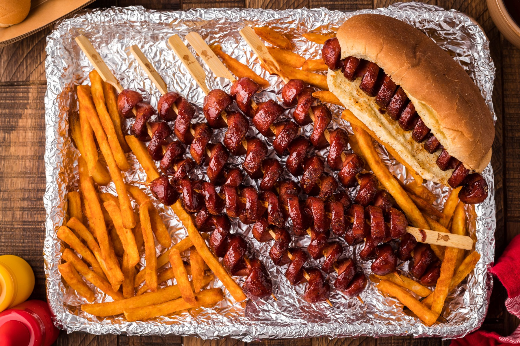 Smoked hot dogs on a foil lined tray with fires and a smoked hot dog in a toasted bun.