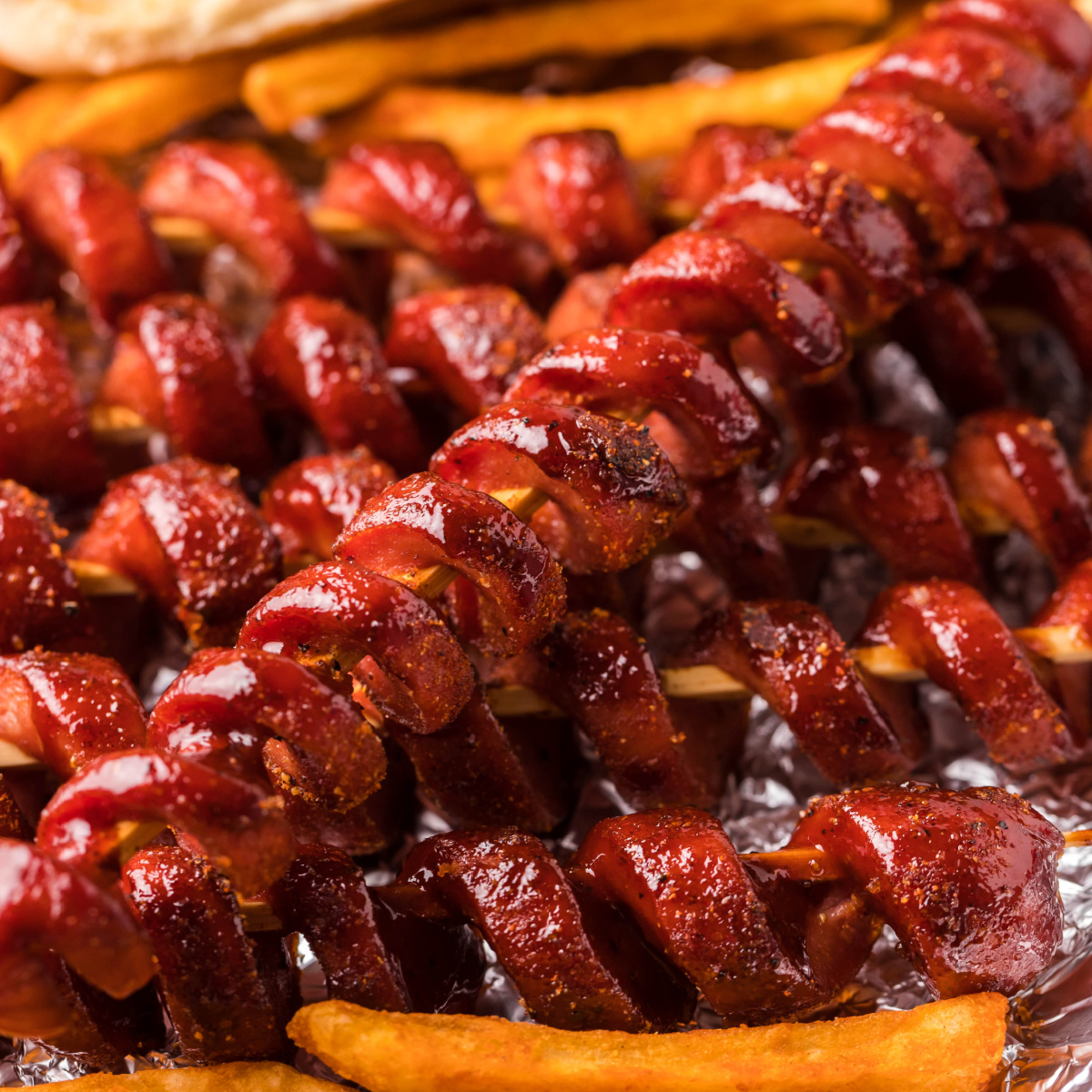 Smoked hot dogs spiraled on wooden skewers.