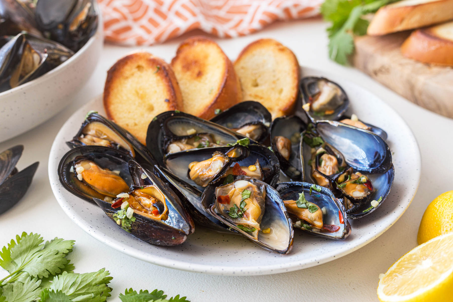 BBQ Thai mussels served on a white plate with slices of toasted baguette bread. 