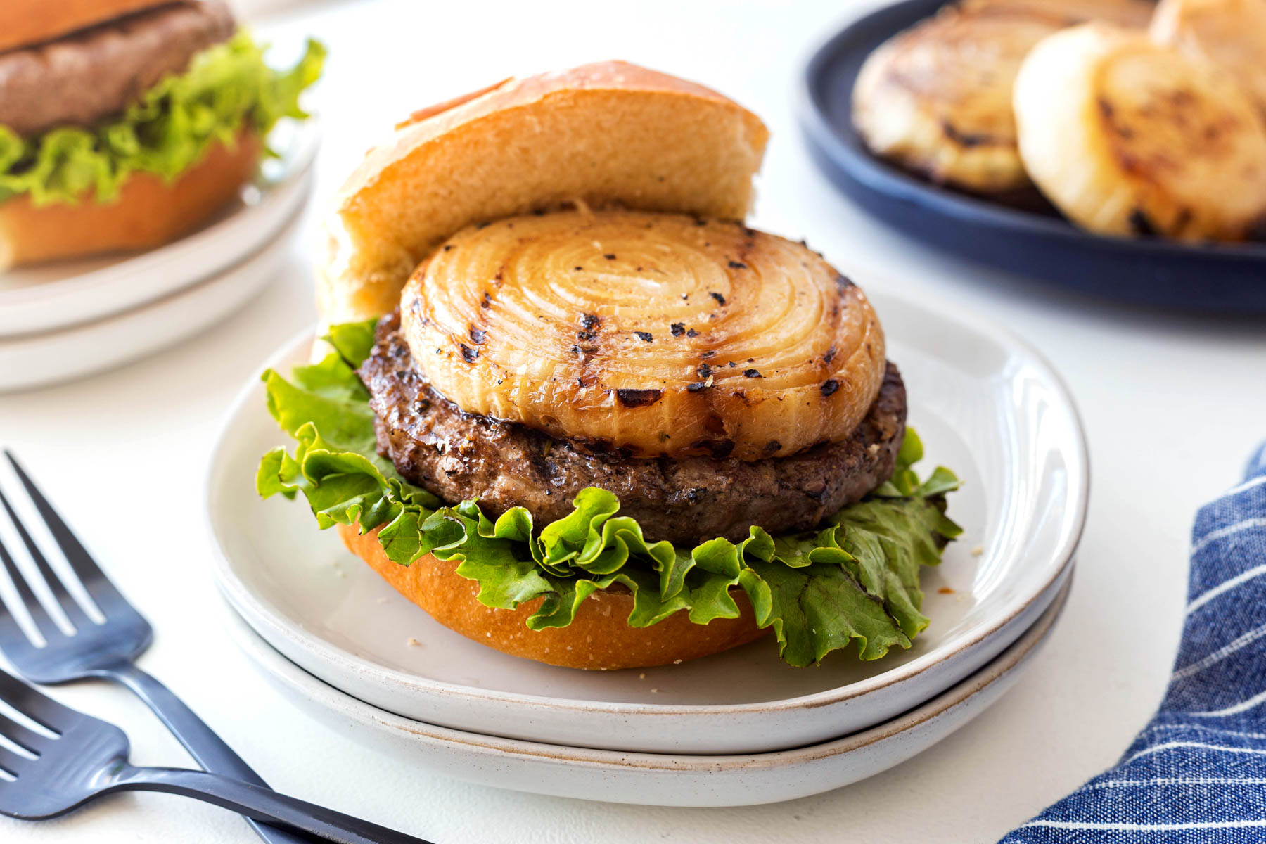 Mustard grilled onion on top of a hamburger sitting on a white plate with lettuce under the burger patty.