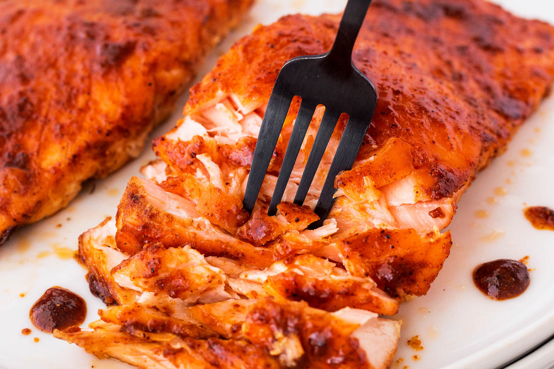 Spicy maple glazed salmon filet on a white plate with a fork separating the flake salmon.