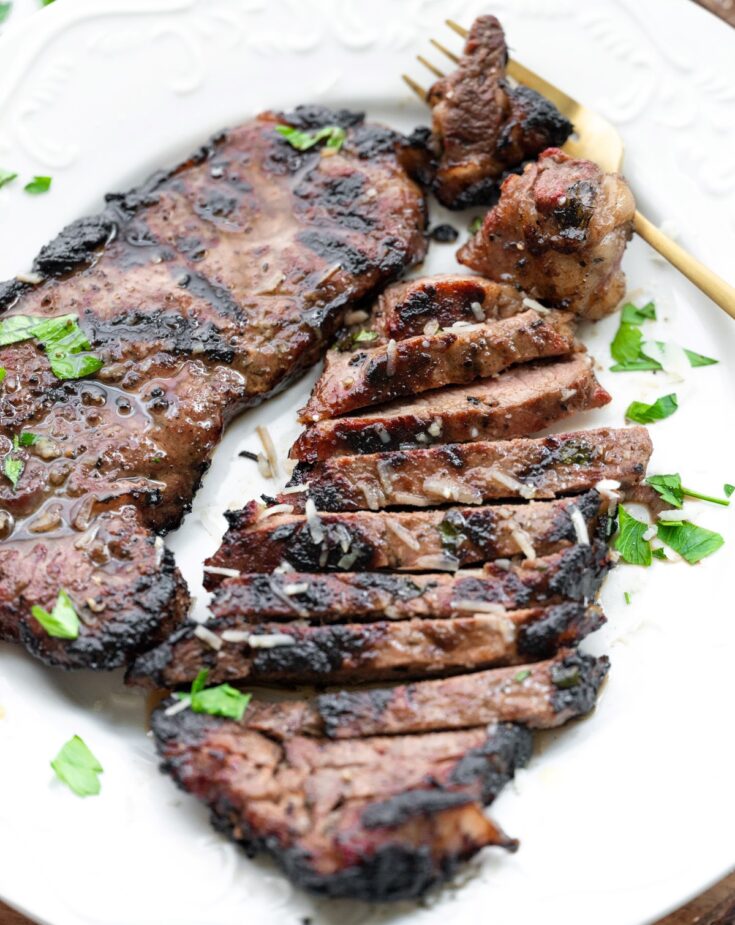 Italian Marinated Smoked Steak sliced on a white plate.