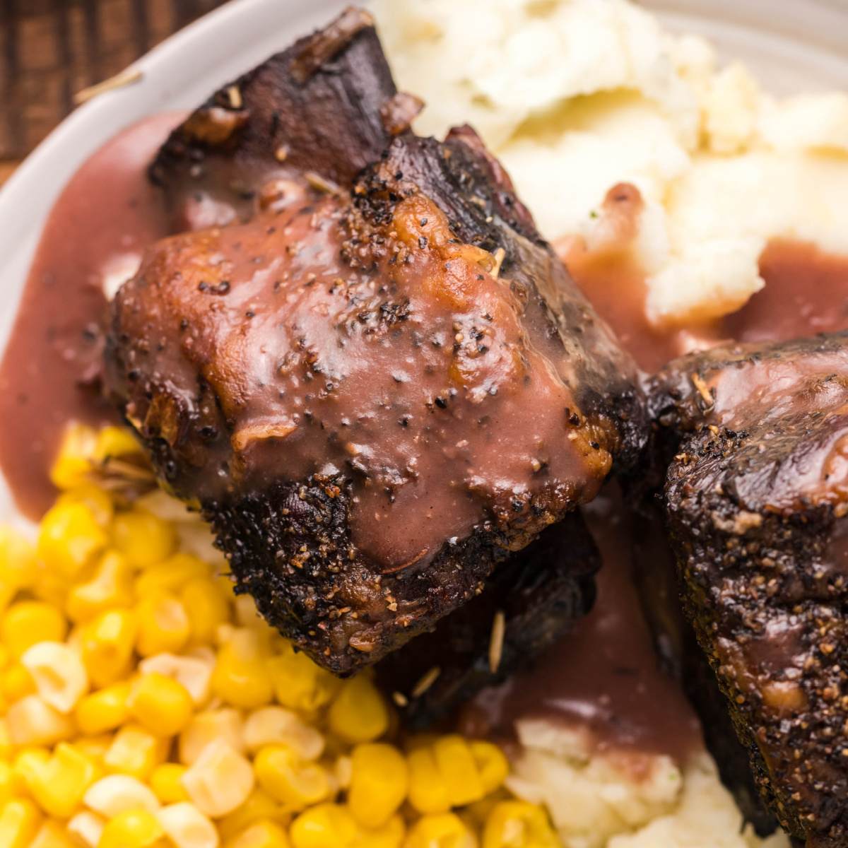 Smoked beef short rib with braising liquid gravy and corn on a plate.