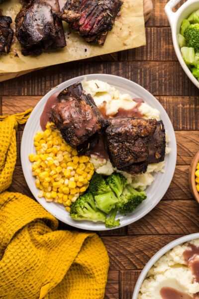 Smoked Beef Short ribs on a plate with mashed potatoes, corn and broccoli.