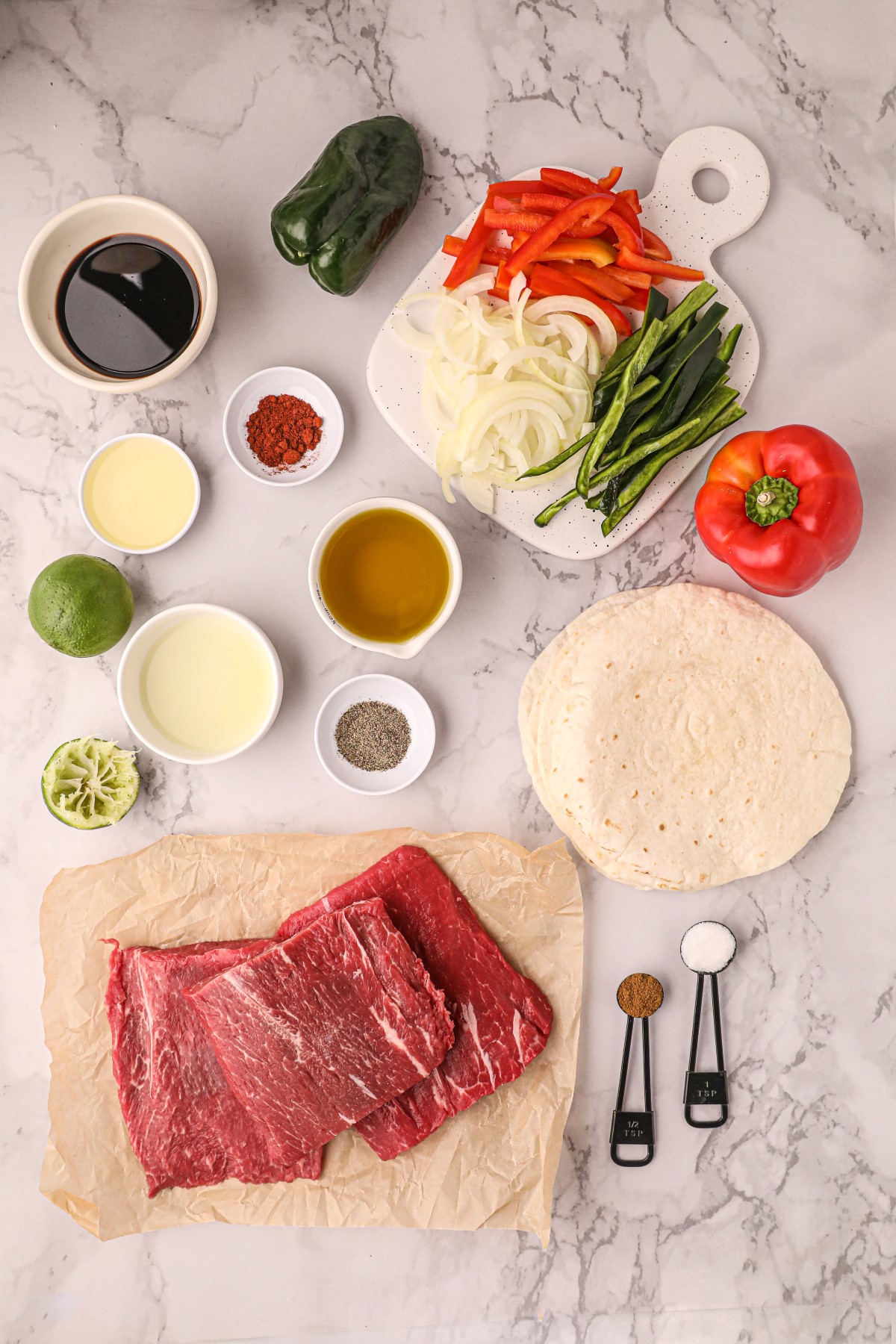 All the ingredients to make skirt steak fajitas laid out on a marble counter top.