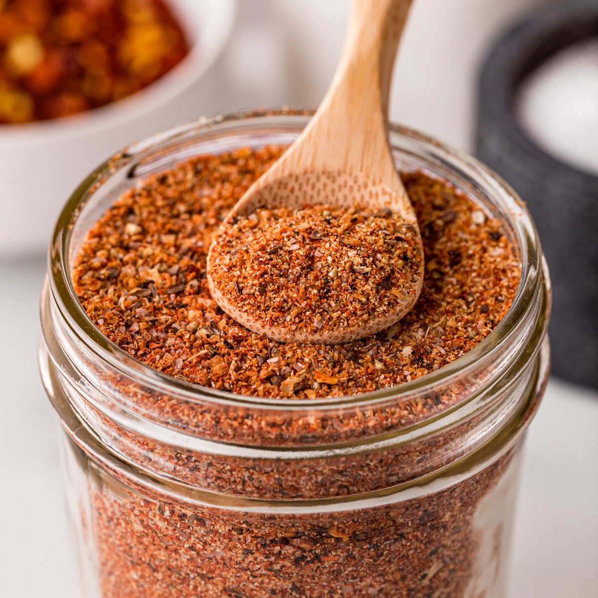 Mason jar filled with Montreal Steak Seasoning and a wooden spoon with a scoop of seasoning.