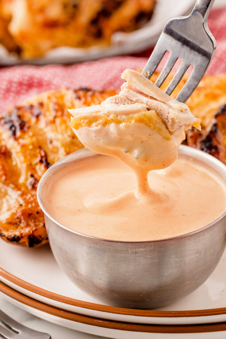 Piece of Chicken on a fork being dipped into a small bowl of Alabama White Sauce