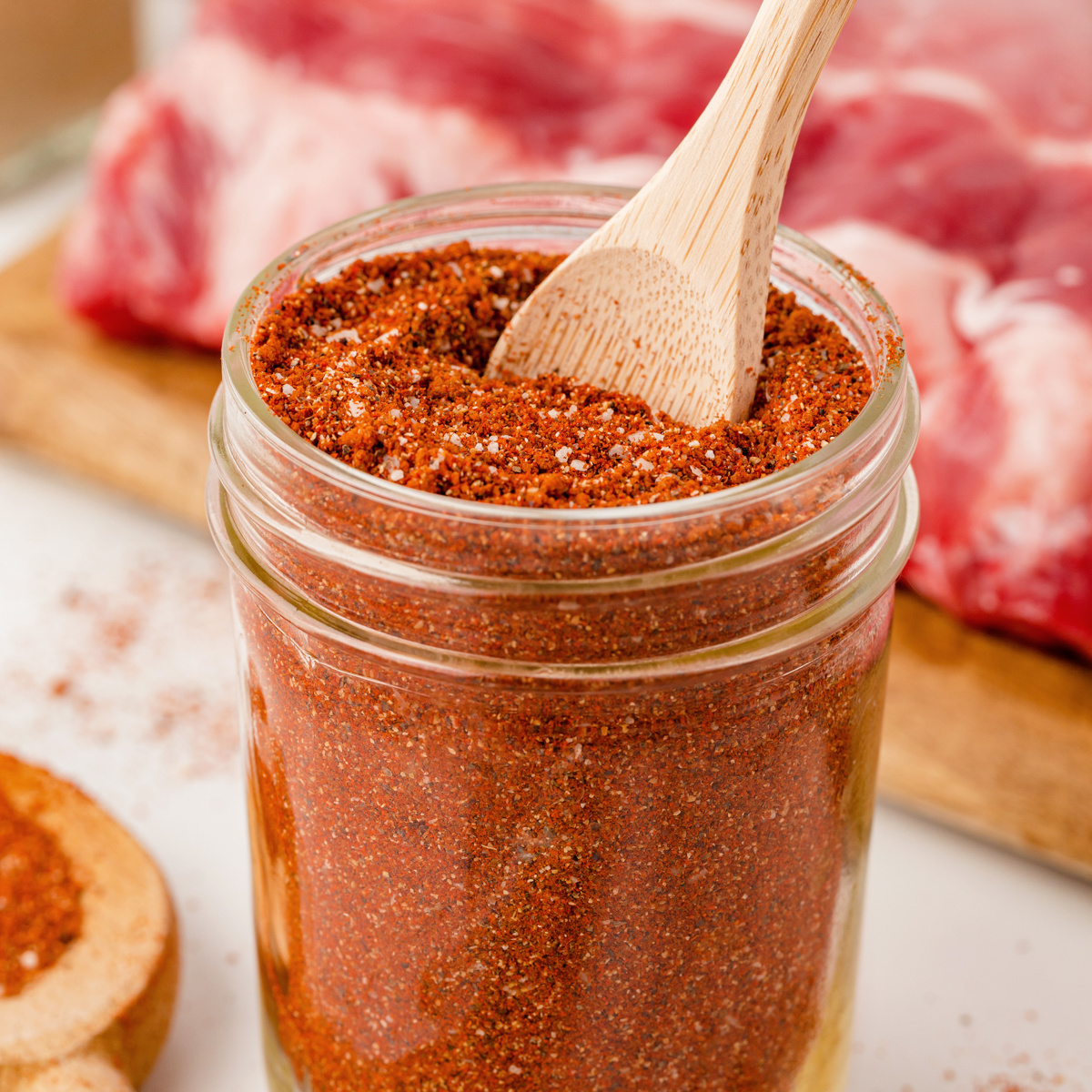 BBQ Rub in a clear glass mason jar with a small wooden spoon in the rub.