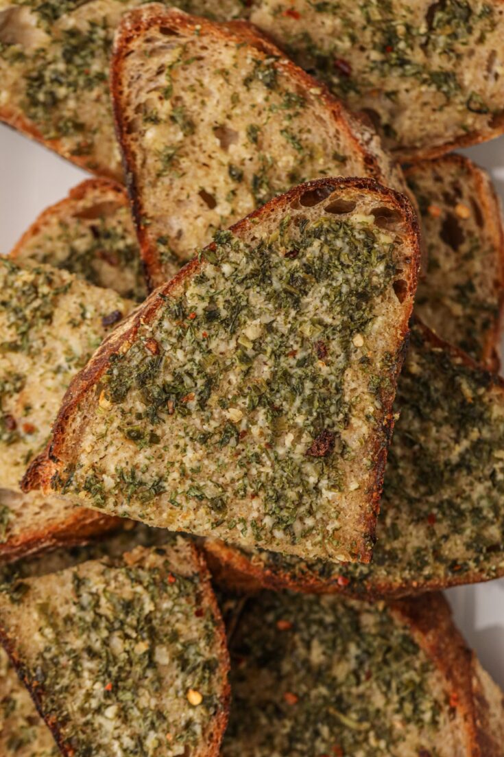 Slices of homemade garlic bread piled on a white plate.