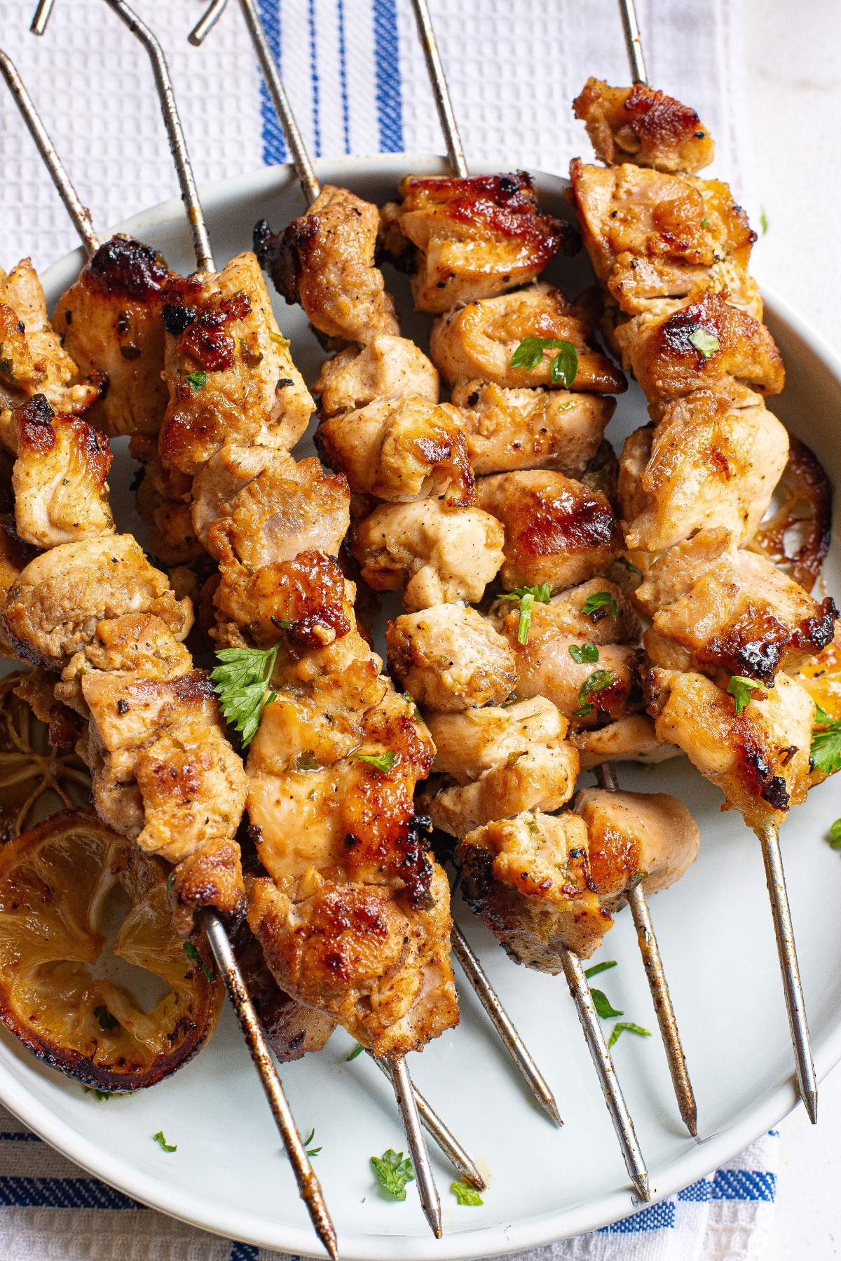 Skewers of Lemon Greek Chicken kabobs served on a plate with lemon slices and chopped parsley.