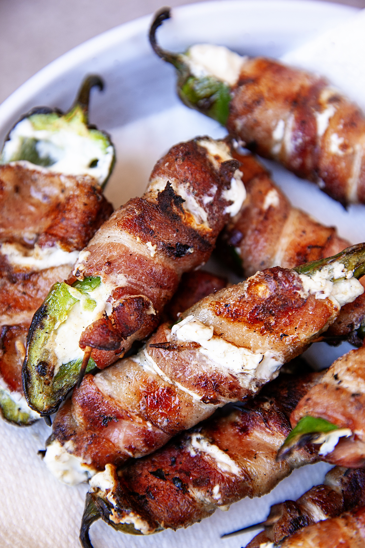 Grilled jalapeno poppers wrapped in bacon on a white serving platter.