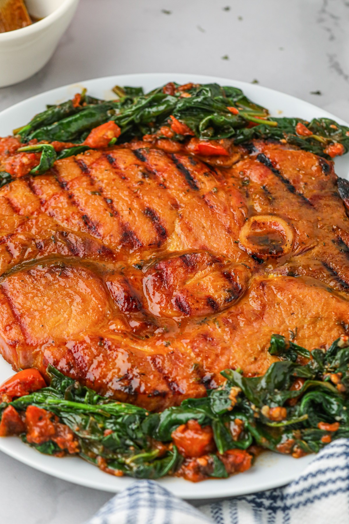 Grilled ham steak on a serving platter with sautéed spinach and tomatoes.