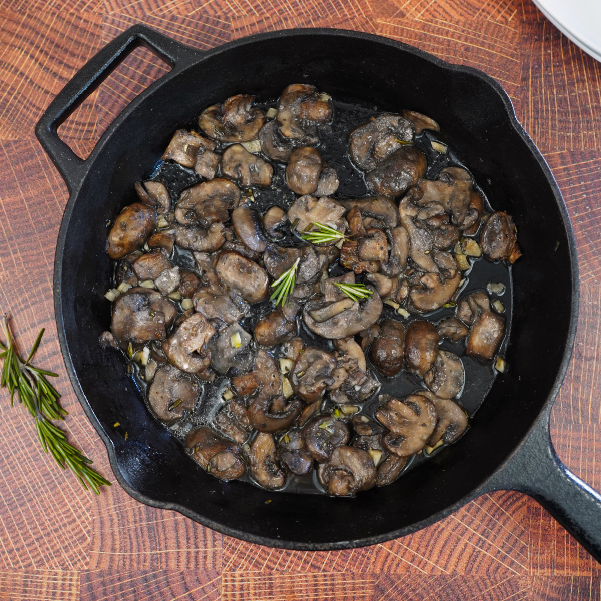 Rosemary smoked mushrooms in a cast iron skillet with fresh rosemary on a wooden board.