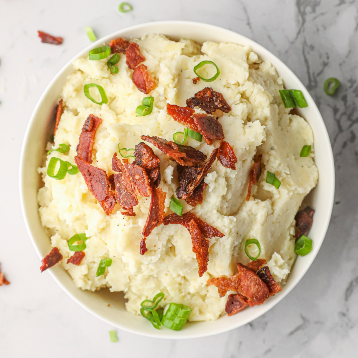 Horseradish Smoked Potatoes in a white bowl garnished with crumbled bacon and chopped green onions.