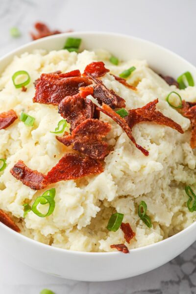 Smoked horseradish potatoes in mashed in a bowl and toped with crumbled bacon and green onions.