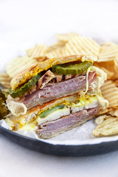 Cubano Sandwich cut in half on a plate with ripple chips.