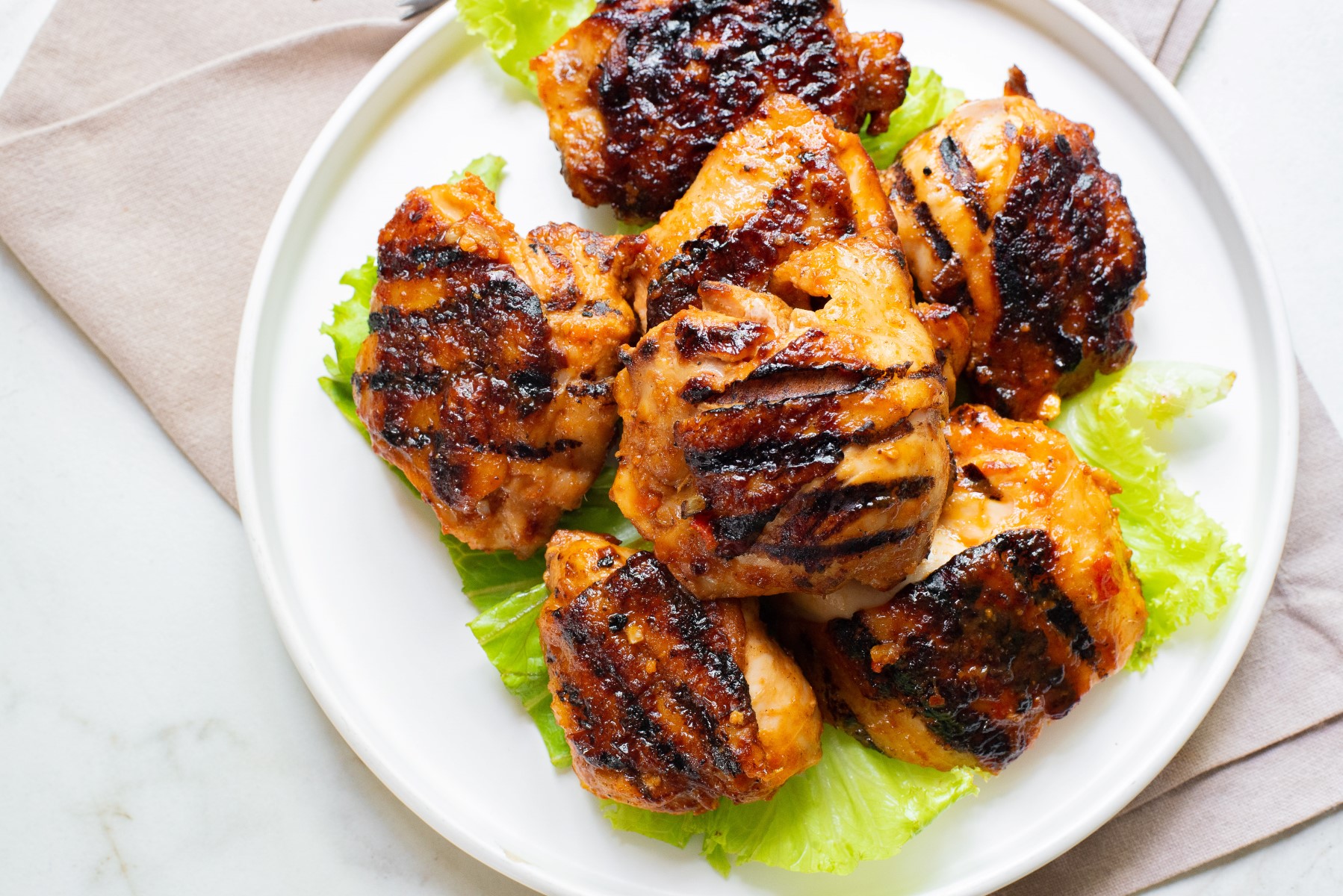 Grilled Harissa Chicken Thighs on a bed of lettuce servind on a white platter.
